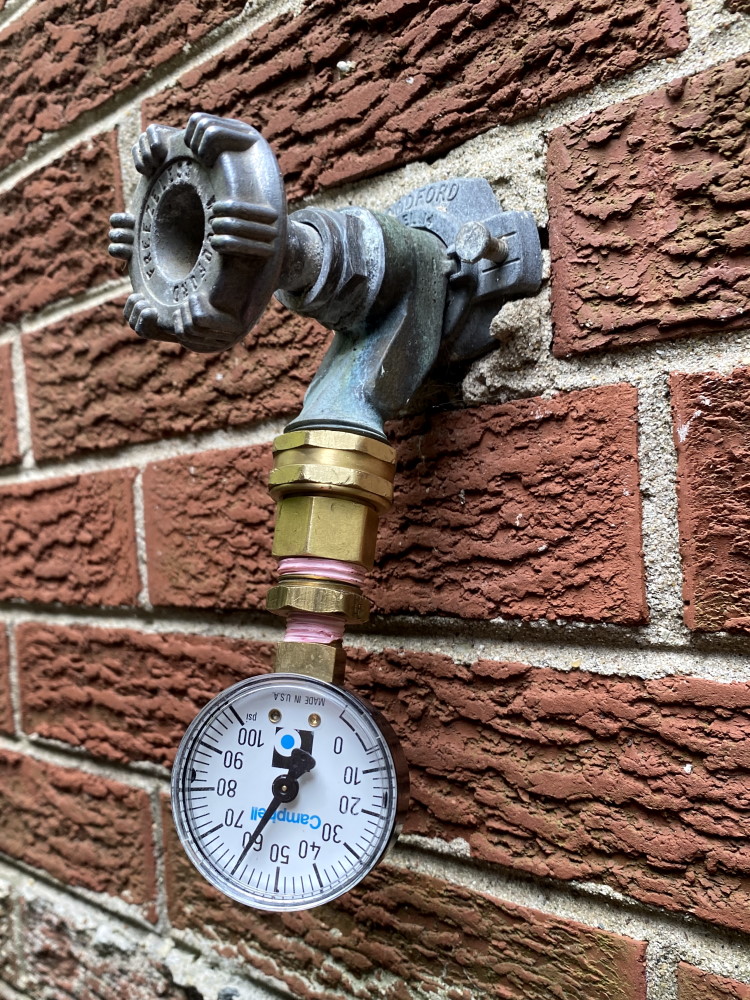 Water pressure gauge attached to hose bib with water on